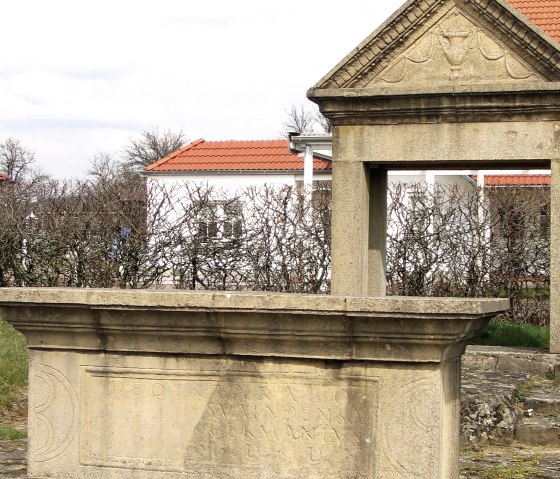 Nachbildung eines gallo-römischen Weihdenkmals mit Inschrift, im Hintergrund moderne Gebäude und kahle Büsche., © Elke Wagner, Felsenland Südeifel Tourismus GmbH Nachbildung eines gallo-römischen Weihdenkmals mit Inschrift, im Hintergrund moderne Gebäude und kahle Büsche., © Elke Wagner, Felsenland Südeifel Tourismus GmbH