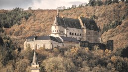 Das Schloss Vianden thront majestätisch auf einem Hügel, umgeben von herbstlich gefärbten Bäumen und einem bewölkten Himmel., © Jengel Das Schloss Vianden thront majestätisch auf einem Hügel, umgeben von herbstlich gefärbten Bäumen und einem bewölkten Himmel., © Jengel