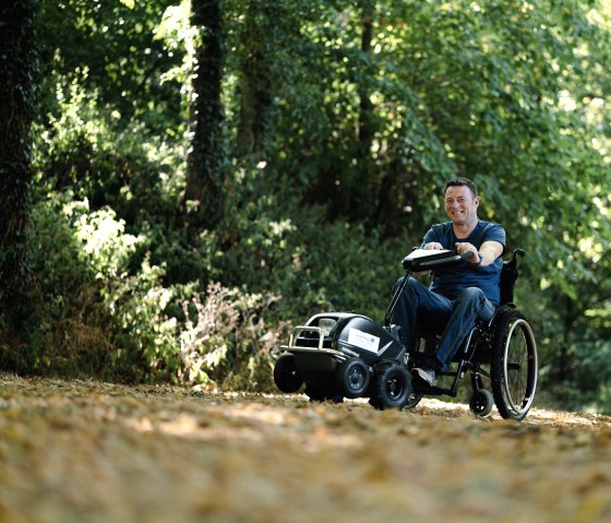 Wheelchair user with wheelchair traction device on a hiking trail in the Southern Eifel Nature Park, © Naturpark Südeifel, Thomas Urbany Wheelchair user with wheelchair traction device on a hiking trail in the Southern Eifel Nature Park, © Naturpark Südeifel, Thomas Urbany