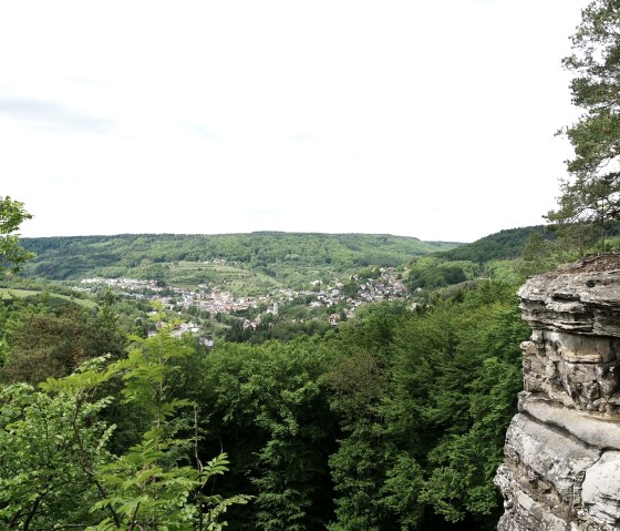 Blick vom Aussichtspunkt oberhalb des Teufelslochs auf Bollendorf, umgeben von grünen Wäldern und Hügeln, mit Felsen im Vordergrund., © Elke Wagner, Felsenland Südeifel Tourismus GmbH