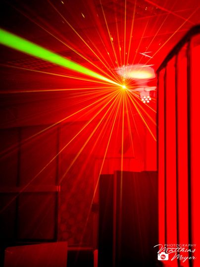 Un spectacle lumineux vivant avec des lasers rouges et verts dans une pièce sombre. L'atmosphère est festive et énergique.