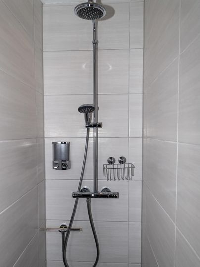 Eine moderne Dusche mit einer Kopf- und Handbrause. Die Wände sind mit hellen Fliesen gefliest.