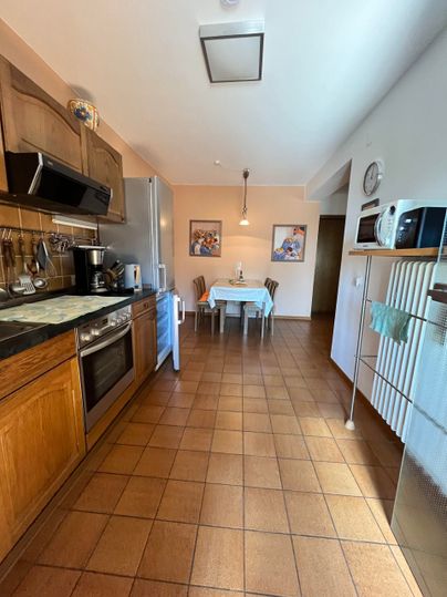 Eine moderne Küche mit Holzschränken und modernen Geräten. Im Hintergrund steht ein Esstisch für vier Personen.