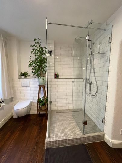 Een moderne badkamer met een glazen douche en witte tegels. Een plant en een houten bank zorgen voor een aangename sfeer.