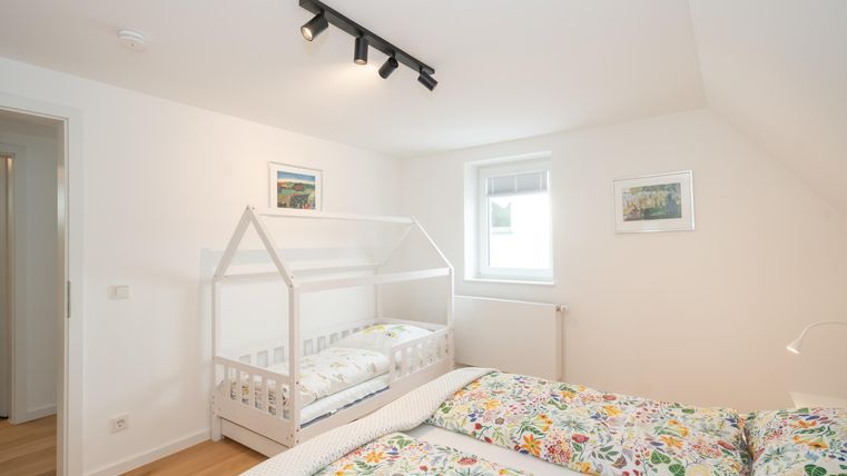Une chambre lumineuse avec un lit double et un lit d'enfant en forme de maison. Les murs sont de couleur claire et décorés avec des images.