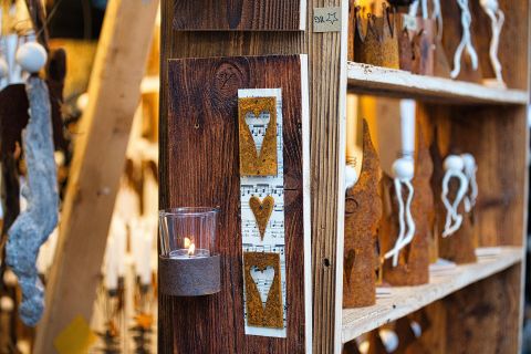Ein Holzregal mit handgefertigten Dekorationsgegenständen und Kerzen. An der Wand hängen rustikale Elemente mit Herzmotiven.