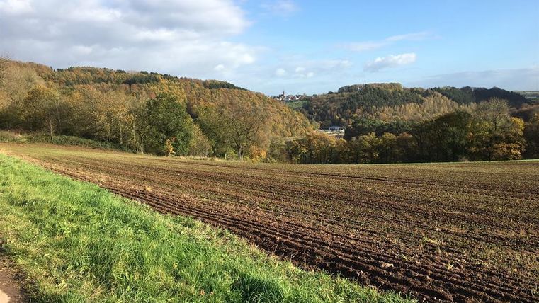 Une vallée boisée avec des collines douces et un champ fraîchement cultivé au premier plan. Le ciel est clair et partiellement nuageux.