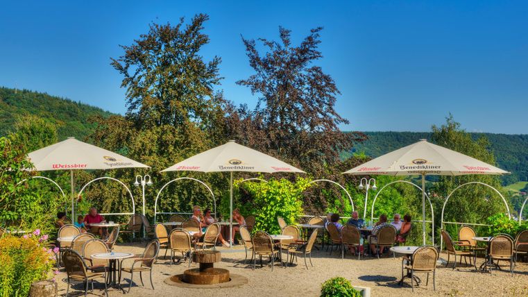 Un café confortable en plein air avec des parasols et de nombreux sièges. Entouré d'arbres verts et d'un paysage pittoresque.