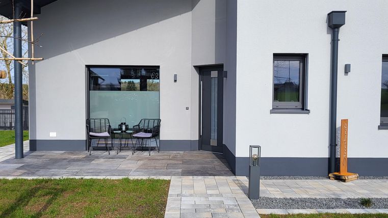 Une maison moderne avec une peinture grise et de grandes fenêtres. Le chemin menant à la porte d'entrée est pavé et traverse une pelouse verte.