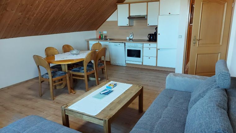 Een lichte, gezellige appartement met een open keuken en een eetgedeelte. De woonkamer is uitgerust met een grijze bank en een houten tafel.