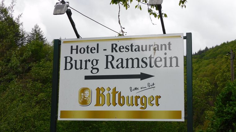 Une enseigne pour le restaurant-hôtel Burg Ramstein. Elle montre une flèche vers la gauche et fait la promotion de la bière Bitburger.
