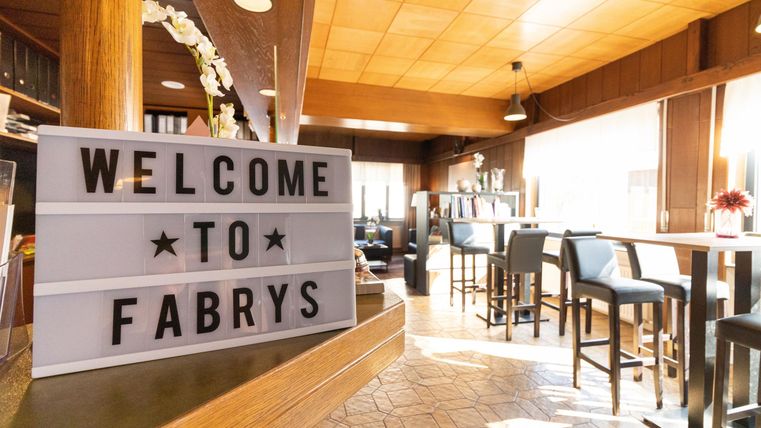 Ein einladendes Restaurant mit einem "Willkommen bei Fabrys"-Schild. Helle Farben und gemütliche Sitzgelegenheiten schaffen eine freundliche Atmosphäre.