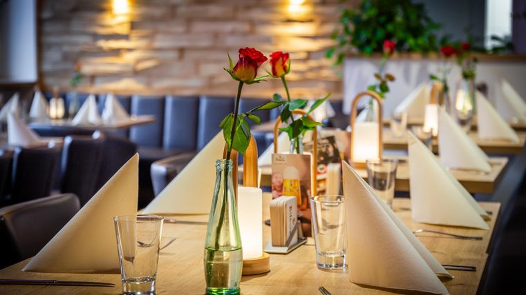 Ein elegantes Restaurant mit schön gedeckten Tischen. Auf jedem Tisch befinden sich rote Rosen und dekorative Tischkarten.