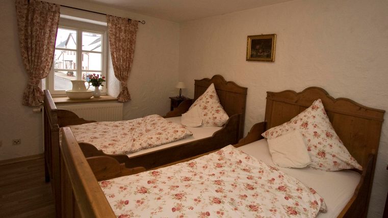 Een gezellig slaapkamer met twee eenpersoonsbedden van hout en bloemige beddengoed. Het raam laat veel licht binnen en biedt uitzicht naar buiten.