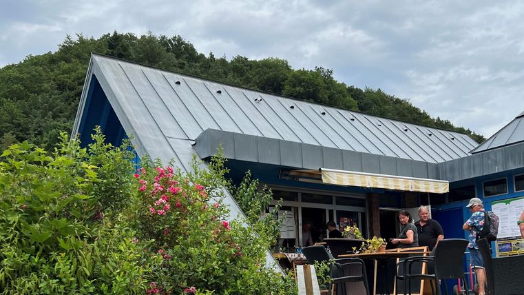 A modern building with a sloping roof in a natural setting. People are standing outside and enjoying the atmosphere.