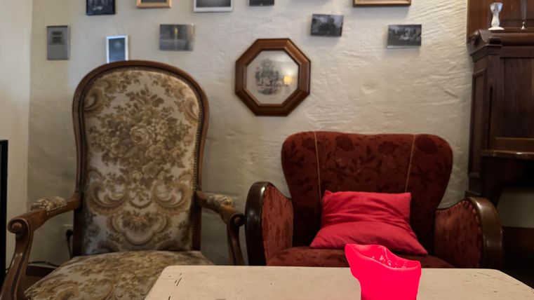 Un ensemble de salon confortable avec deux fauteuils et une table. Sur le mur, différents cadres photo sont accrochés et une bougie rouge se trouve sur la table.