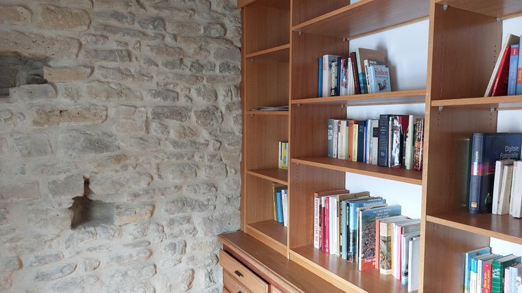 Een boekenplank vol boeken staat naast een stenen muur. De omgeving is gezellig en uitnodigend.