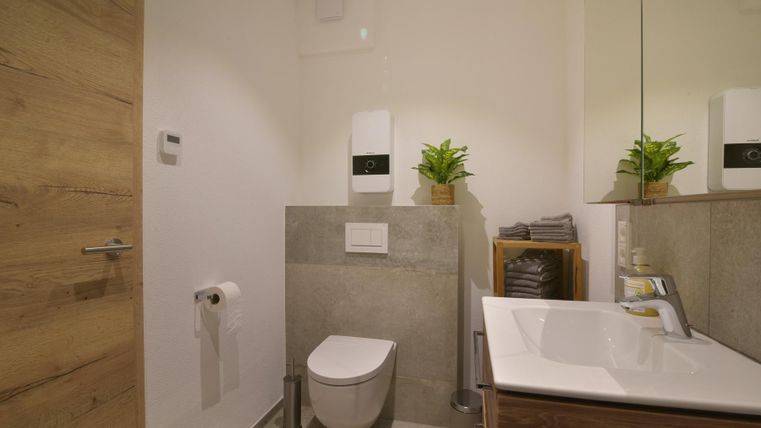 Een moderne badkamer met een toilet en een wastafel. De muren zijn in neutrale kleuren gehouden en er zijn enkele planten ter decoratie.