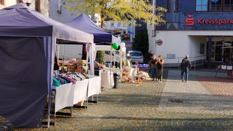 Ein Wochenmarkt mit mehreren Ständen und bunten Zelten. Leute schlendern entspannt die Straße entlang.