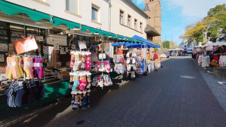 Ein Markt mit bunten Ständen bietet eine Vielzahl von Kleidung und Accessoires an. Die Straße ist lebhaft und gut besucht.