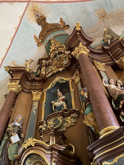 Een prachtig altaarretabel met artistieke beelden en gouden versieringen. Op de achtergrond zijn schilderachtige plafondschilderingen te zien.