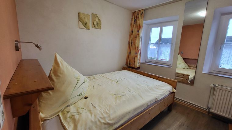 A cozy bedroom with a single bed and warm colors. Large windows bring plenty of light into the room.