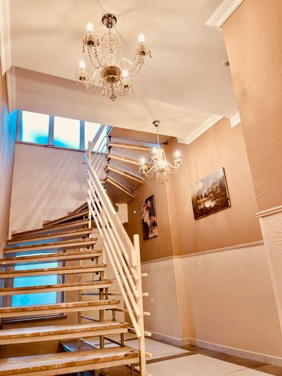 Un élégant escalier avec un escalier en bois ouvert et deux lustres modernes. Des œuvres d'art sont accrochées aux murs, tandis que beaucoup de lumière naturelle pénètre par une grande fenêtre.