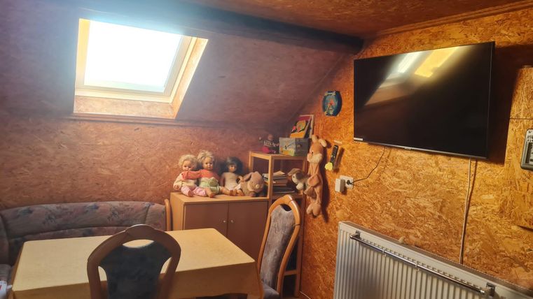 A cozy room with a table and chairs. A skylight lets in daylight, and a TV hangs on the wall.