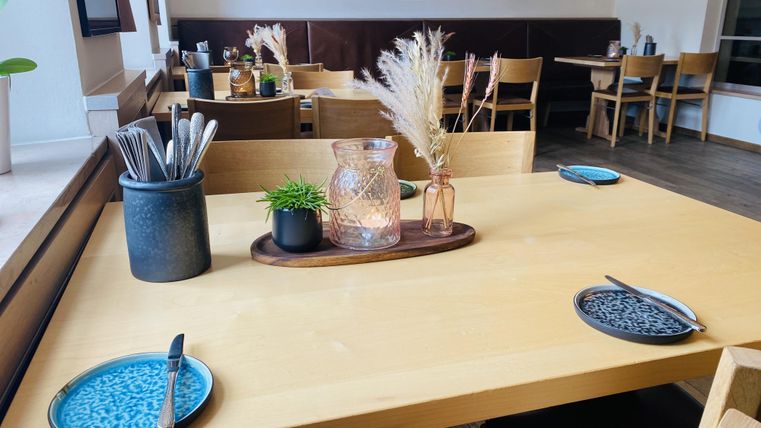 A cozy restaurant table with blue plates and cutlery. In the background, additional tables and modern decor can be seen.