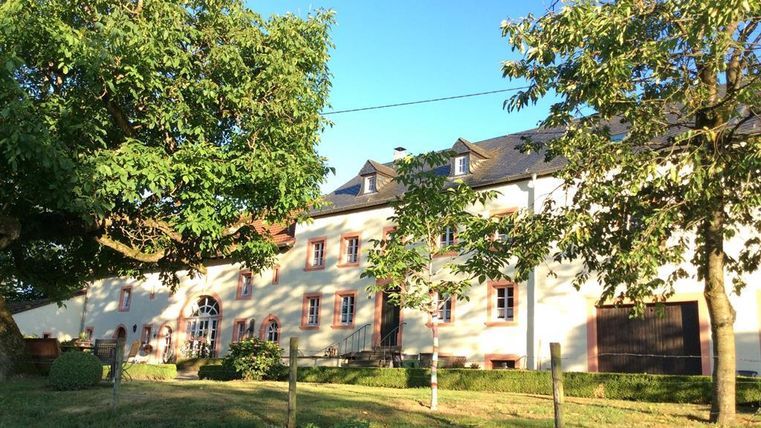 Un grand bâtiment lumineux avec des fenêtres rouges et un beau jardin. Autour de la maison, des arbres verts poussent et le ciel est clair et bleu.