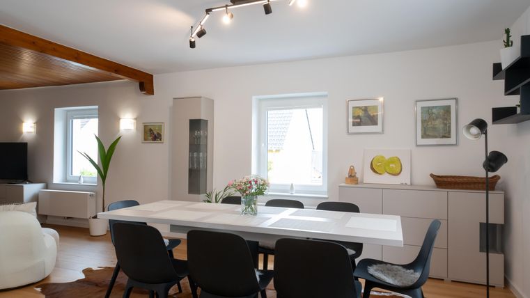 Une salle à manger moderne avec une grande table blanche et des chaises noires. Les murs sont peints en clair et décorés avec des œuvres d'art.