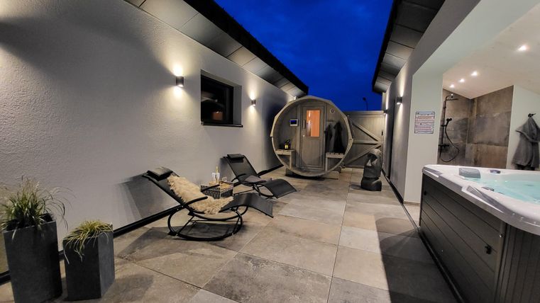 Une terrasse moderne avec des transats et un jacuzzi. L'environnement est élégant et offre une atmosphère relaxante la nuit.