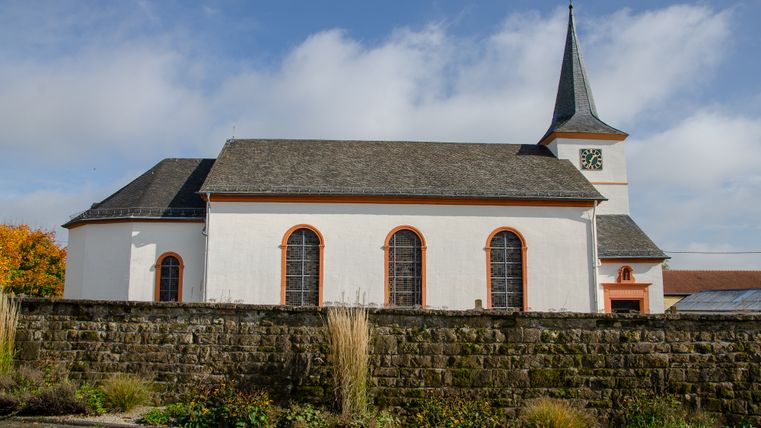 Pfarrkirche St. Martin in Dockendorf mit Uhrturm und blühendem Garten im Vordergrund.