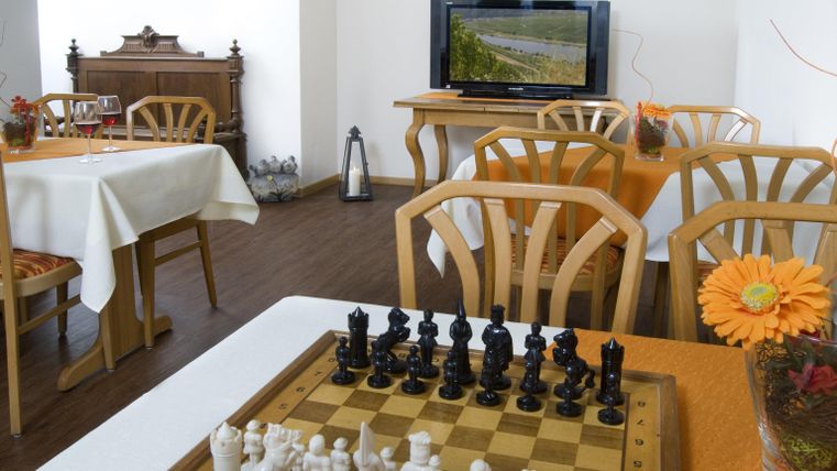 Une pièce confortable avec un échiquier et une fleur décorative sur la table. En arrière-plan, des tables et une télévision sont visibles.