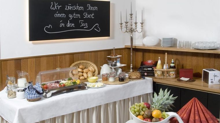 Een buffet met een verscheidenheid aan ontbijtaanbiedingen, waaronder broodjes, fruit en verschillende smeersels. Op de achtergrond staat een bord met de wens voor een goede start van de dag.