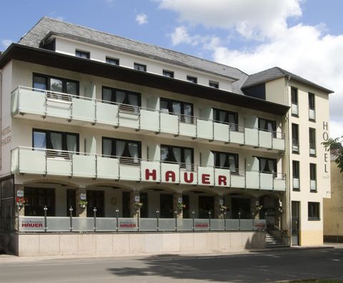 Ein modernes Hotelgebäude mit einem klaren Design. Die Fassade hat große Fenster und Balkone, beschriftet mit "HAUER".