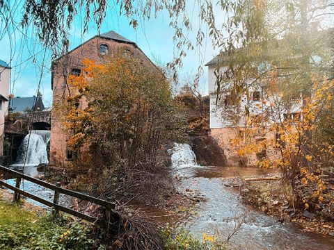 Een schilderachtig landschap met oude gebouwen en watervallen. De bomen zijn kleurrijk en het water stroomt rustig voorbij.