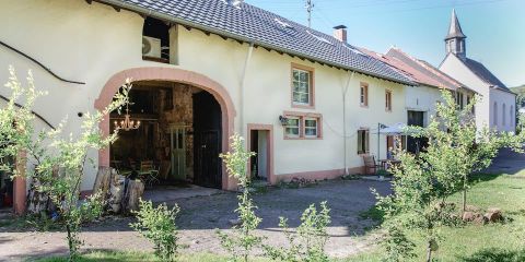 Ein traditionelles Bauernhaus mit einem großen Tor und einigen Fenstern. Im Vordergrund wachsen kleine Pflanzen auf dem Grundstück.