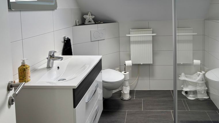 Ein modernes Badezimmer mit weißen Fliesen und einem großen Spiegel. Es gibt eine Dusche, ein Waschbecken und ein WC.