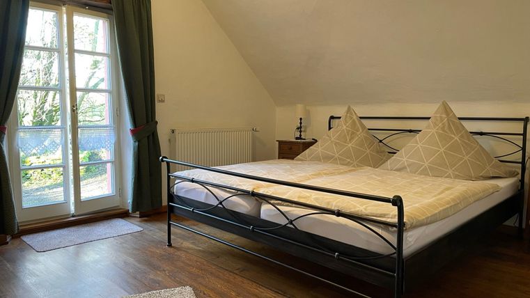 Une chambre confortable avec un grand lit et deux coussins.
Des fenêtres avec des rideaux laissent entrer la lumière du jour.