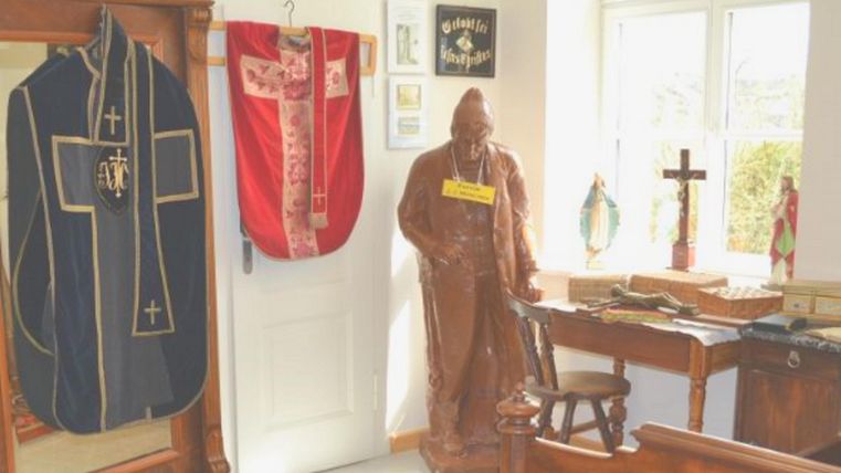 A traditional room with religious objects. Robes hang on the wall and a statue stands on a table.