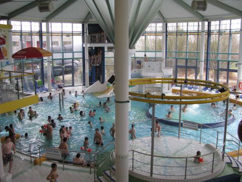 Een waterpark met veel mensen die in het water spelen. Glijbanen en verschillende waterattracties zijn zichtbaar.