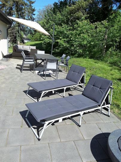 Eine gemütliche Terrasse mit zwei Liegen und einem Essbereich. Grüne Bäume und helles Wetter schaffen eine entspannte Atmosphäre.