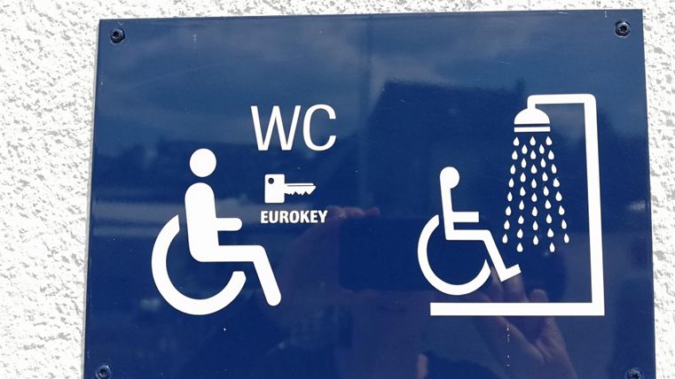 Een bord met de tekst "WC" en een Eurokey-symbool. Het toont symbolen voor een toegankelijk toilet en een douche.