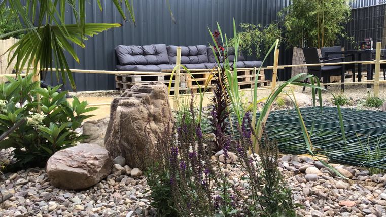 Ein moderner Garten mit Kies, Steinen und verschiedenen Pflanzen. Im Hintergrund stehen gemütliche Sitzgelegenheiten.