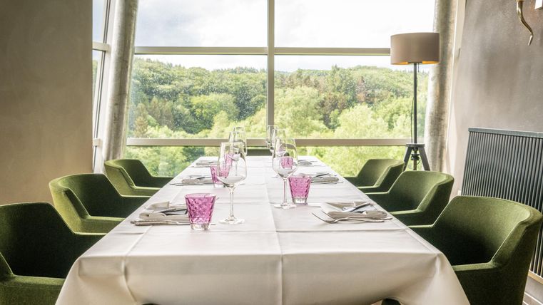 Un espace de repas élégant avec une longue table et des chaises vertes confortables. La grande baie vitrée offre une vue sur le jardin.