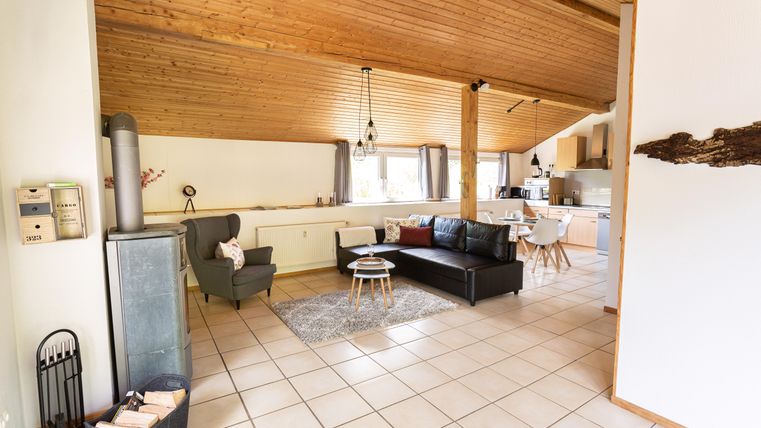 A cozy living room with a wooden ceiling, modern furniture, and bright colors. The open kitchen is clearly visible, and there is a dining area with a table and chairs.