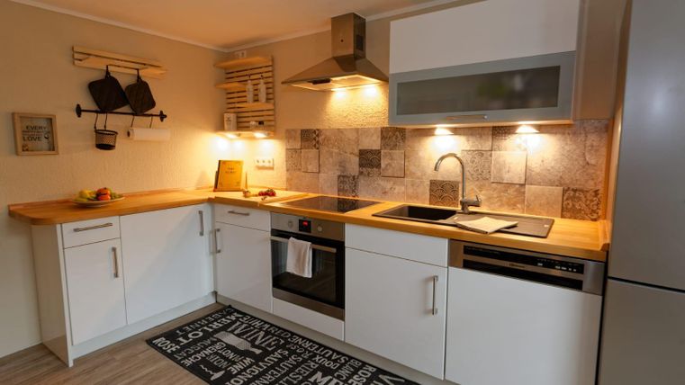 Une cuisine moderne avec un plan de travail en bois et des armoires blanches. Elle dispose d'une cuisinière, d'un évier et d'un choix de carrelage attrayant.