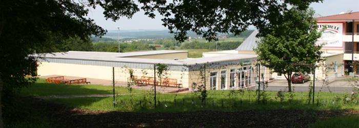 Een modern gebouw, omringd door bomen en met een wijd uitzicht op het landschap. Het terras nodigt uit tot verblijven.