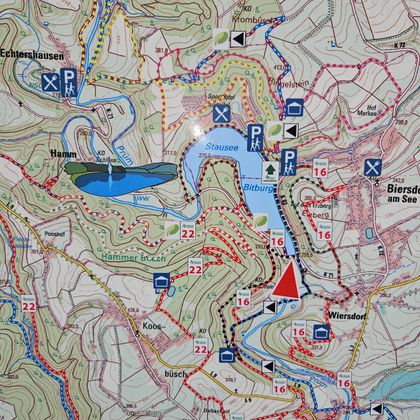 Een gedetailleerde wandelkaart met verschillende paden en gemarkeerde punten. Het toont ook een meer en parkeermogelijkheden in de omgeving.